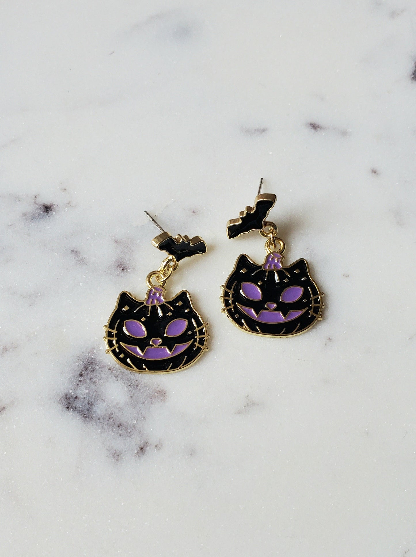 Cat-shaped earrings with purple accents on a marble surface