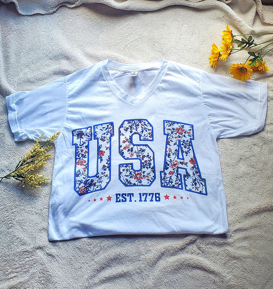White t-shirt with 'USA' design on a gray blanket by a window