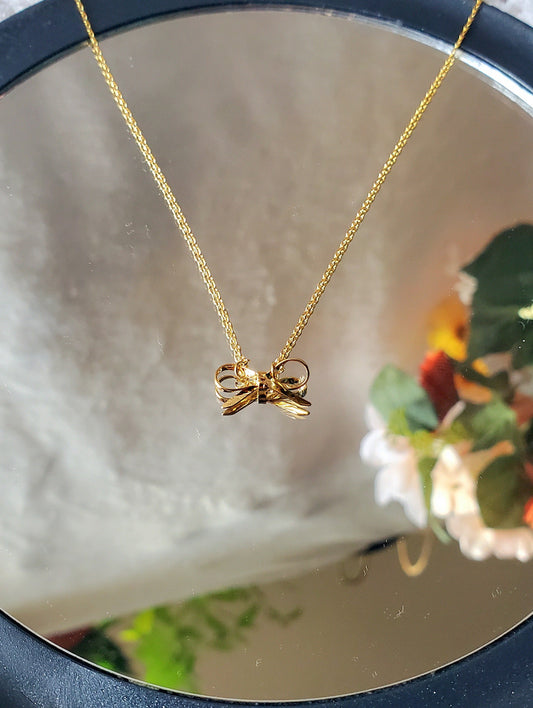 Gold necklace with a bow pendant on a mirror surface