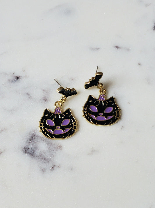 Cat-shaped earrings with purple accents on a marble surface